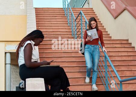 One student is walking down the stairs and other is watching her phone Stock Photo