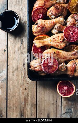 Baked chicken drumstick with orange on a wooden background, top view. Stock Photo