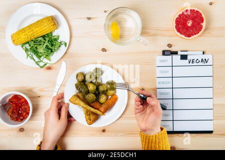 Top view Woman eating her portion of baked vegetables as brussels sprouts, parsley root, carrots acording to her vegan menu on daily board. New Stock Photo