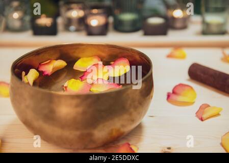 Tibetan singing bowl with floating in water flower petals. Special sticks, burning candles, petals on the wooden background. Meditation and Relax Stock Photo