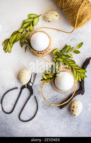 Eggs in egg cups and quail eggs with boxwood leaves, string and scissors Stock Photo