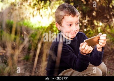 A nice boy in a forest is amazed when he sees a funny video on his mobile  phone Stock Photo - Alamy