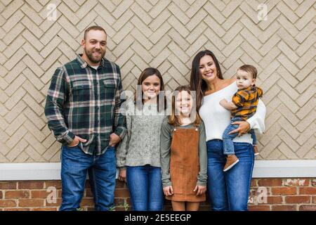 A family of five with two girls and a baby boy standing in front of a brick herringbone Stock Photo