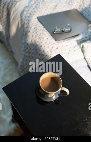 Coffee break working from home concept closed laptop sits on bed with glasses and cup of coffee on side table nightstand night table  shot from Stock Photo