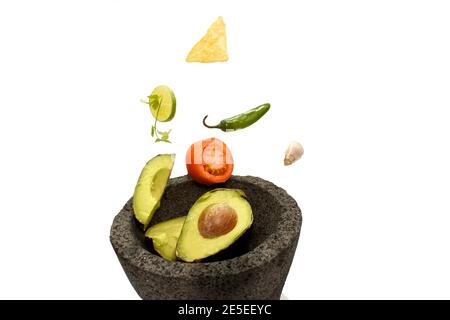 Ingredients for avocado dip flying and falling in stone bowl lemon, coriander, chili, garlic, tomato, sliced ​​and nachos Stock Photo