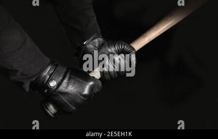 In the dark, two gloved hands hold a baseball bat firmly with the obvious aim of causing mayhem. Stock Photo