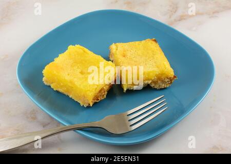 Two baked lemon dessert bars on blue snack plate with fork Stock Photo