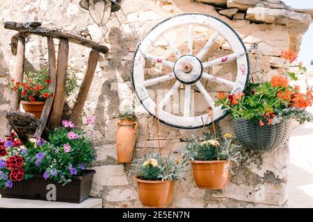 Wooden wheel from a cart in a garden interior. Country style photo zone with petunia and geranium flowers in flower pots. Stock Photo