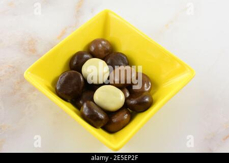 Kruidnoten cookies covered with variety of milk chocolate, dark chocolate and white chocolate in yellow snack bowl on table Stock Photo