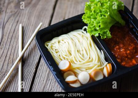 Food delivery in take away boxes package on wooden table at home, Service food order online delivery Spaghetti italian pasta and tomato sauce with sau Stock Photo