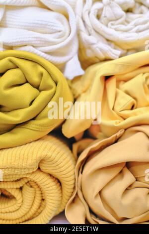 Clothes of yellow shades rolled up. Swirls of various items of female apparel. Close up view. Save space storage. Monochrome garment. Trendy color of spring and summer. Closet arranging.  Stock Photo