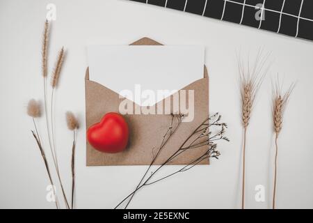 Blank white paper is placed on open brown paper envelope with red heart, Many kinds of dried flowers, Black cloth on white background. Valentine's day Stock Photo