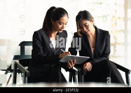 Two Businesswoman discuss to working with using tablet and for searching information stock market chart for trading to Make a profit. Planning and Stock Photo
