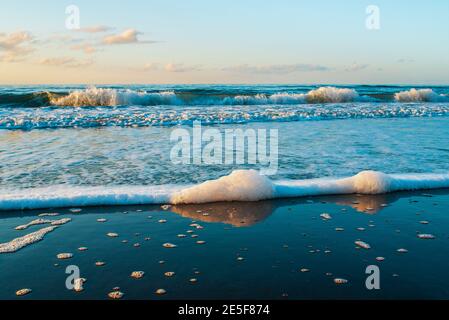 Beautiful sea, sandy beach, seafoam, and clear blue sky on sunset. Natural landscape background with copy space.