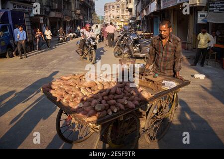 A mobile vendor pushes his cart laden with sweet potatoes or yams across a street in Mumbai, India Stock Photo