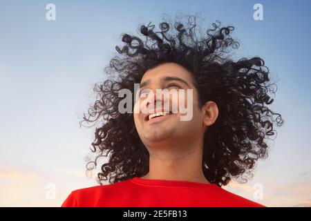 A HAPPY YOUNG MAN WITH CURLY HAIR LOOKING AWAY AND SMILING Stock Photo