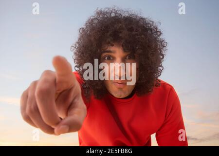 A YOUNG MAN WITH CURLY HAIR POINTING FINGER TOWARDS CAMERA Stock Photo
