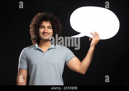 A CURLY HAIRED YOUNG MAN HOLDING THOUGHT BUBBLE AND SMILING AT CAMERA Stock Photo