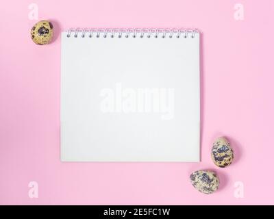 a blank sheet of paper surrounded by quail eggs on a pink background Stock Photo