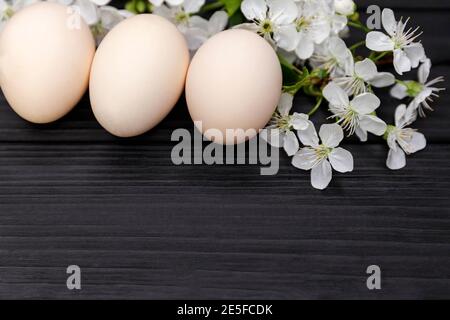 Uncolored easter eggs with cherry flowers branch on wooden background Stock Photo
