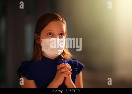Pray for coronavirus victim. Child in face mask praying for sick. Patient in hospital chapel or church during Covid-19 outbreak. Virus pandemic. Peopl Stock Photo
