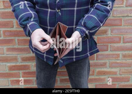 Man with no money showing empty wallet with brick wall behind Stock Photo