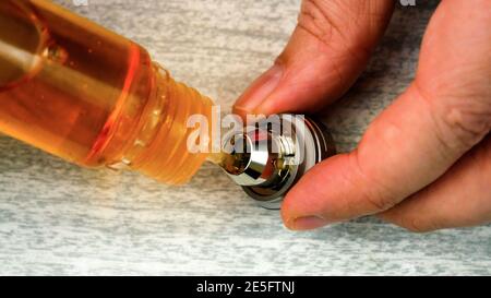 Hands filling e-cig atomizer for vaping with e-liquid - filling directly into the coil head Stock Photo