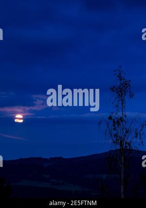 Landscape at blue hour time with clouds and moonrise behind the clouds Stock Photo