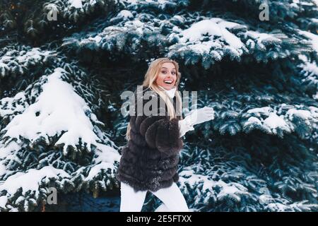 Smiling woman weared in fur coat walks in winter snowy forest. Stock Photo
