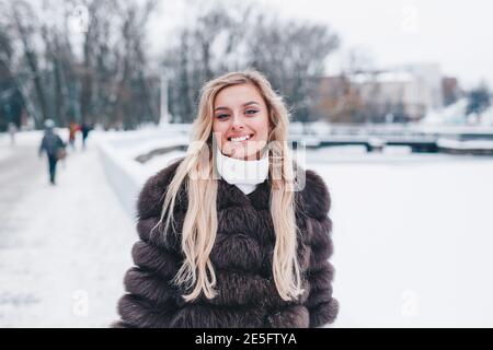 Smiling woman weared in fur coat walks in winter snowy park Stock Photo
