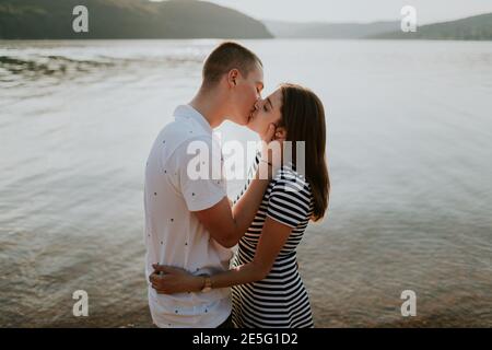 Close up of couple in love kissing at the lake at sunset. Portrait of boyfriend and girlfriend hugging and kissing on the beach on warm summer evening Stock Photo