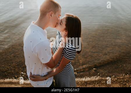 Close up of couple in love kissing at the sea at sunset. Portrait of boyfriend and girlfriend hugging and kissing on the beach on warm summer evening. Stock Photo