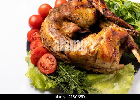 Rabbit meat baked with vegetables and herbs on a plate on a black white background. With tomatoes and lettuce. Stock Photo