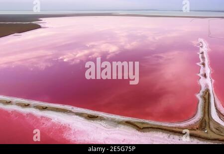Pink lake and shore along the water. Reflection of sky clouds in pink water. Stock Photo
