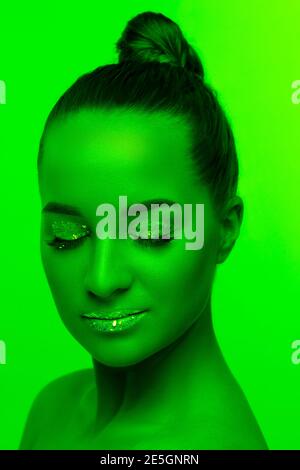 Make up. Handsome woman's portrait isolated on green studio background in neon light, monochrome. Beautiful female model. Concept of human emotions, facial expression, sales, ad, fashion and beauty. Stock Photo