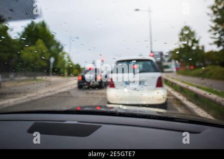 Defocused view at the front driving cars seen through the glass windshield covered with rain drops - traffic jam Stock Photo