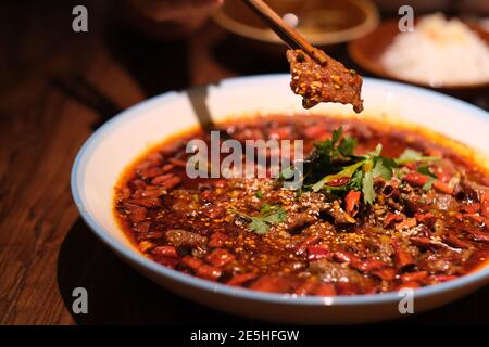 close up chopsticks picking up poached sliced beef in hot chili oil on dinner table. Famous Sichuan cuisine Stock Photo