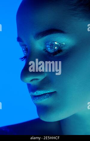 Make up. Handsome woman's portrait isolated on blue studio background in neon light, monochrome. Beautiful female model. Concept of human emotions, facial expression, sales, ad, fashion and beauty. Stock Photo