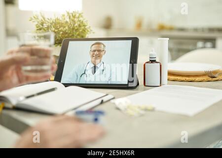 Black tablet with image of a medical worker smiling while video-calling his eldelry patient Stock Photo