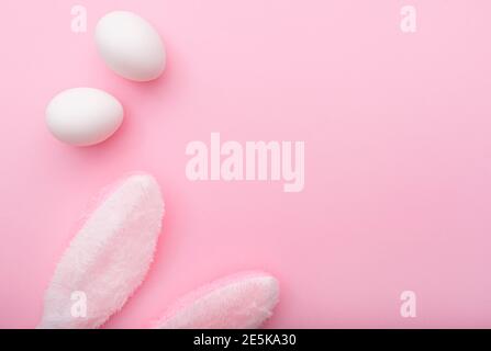 White eggs and rabbit ears on pink background, Easter minimal flat lay, top view, space for text Stock Photo