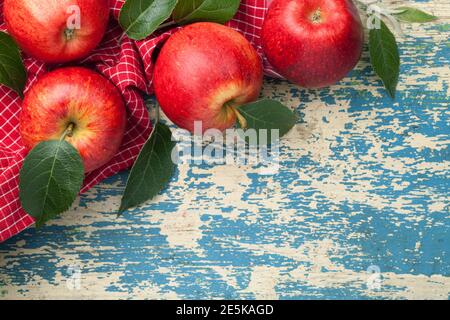 Red apples, fresh green leaves composition on red and white checkered tablecloth. Copy space on wooden background. View from above Stock Photo