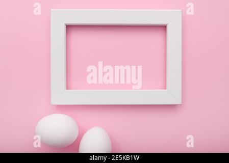 White frame and eggs on pink background, Easter minimal flat lay, top view, space for text Stock Photo