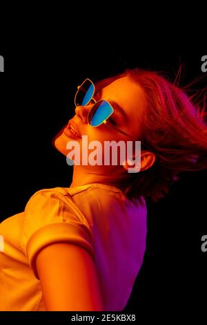 Chill. Caucasian woman's portrait on black studio background in orange-pink neon light. Beautiful female model with blowing hairs out. Concept of human emotions, facial expression, sales, ad, fashion. Stock Photo