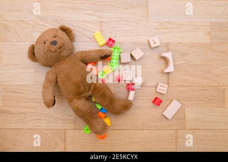 Scattered on wooden floor children's toys, plastic blocks,  construction set and teddy bear in the children's room Stock Photo