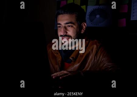 Young man in the overtime in the dark from his office working hard on his project with a smile look on his face Stock Photo