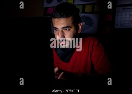 Young man in the overtime in the dark working hard  from his office on his project with a serious look on his face Stock Photo