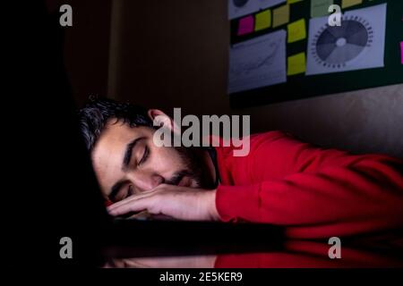 Young man is sleeping in his dark office after long term of working and overtime in front of his laptop Stock Photo