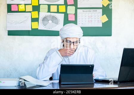 Young arabian man is occupied with his work from his home with high concentration using his laptop with sticky board in his office Stock Photo