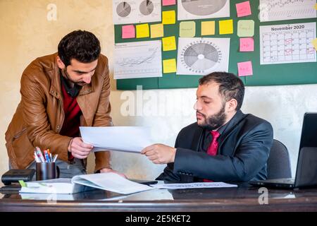 Young man providing some work papers to another man wearing suit on his desk t get the right service or support Stock Photo