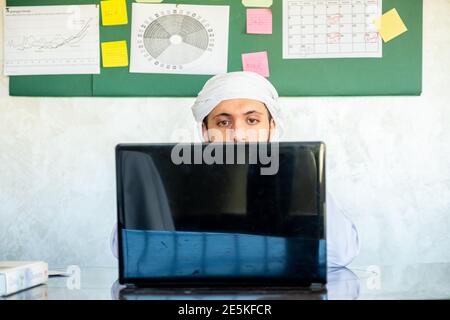 Young arabian man is occupied with his work from his home with high concentration using his laptop with sticky board in his office Stock Photo